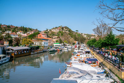 Boats moored in canal amidst buildings against clear blue sky