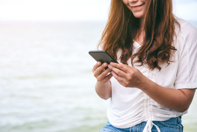 Young woman using mobile phone against sea