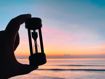 Silhouette person holding sea against sky during sunset