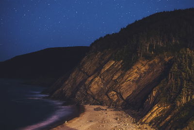 Rocky mountains by sea against sky at night