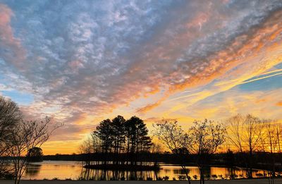 Silhouette trees by lake against romantic sky at sunset