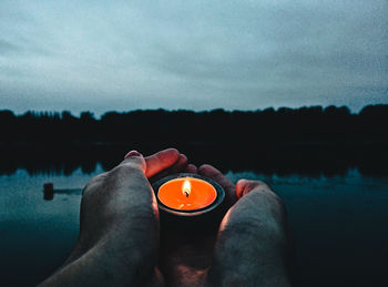 Man with candle by lake against sky
