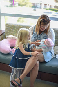 Mother and daughter playing with baby girl on sofa at home