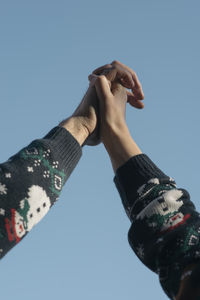 Low angle view of couple holding hands against clear sky