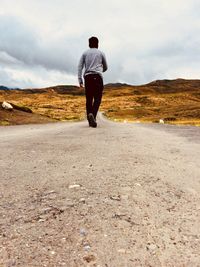 Rear view of man walking on road against sky