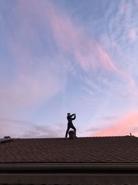 Low angle view of man standing on roof against sky