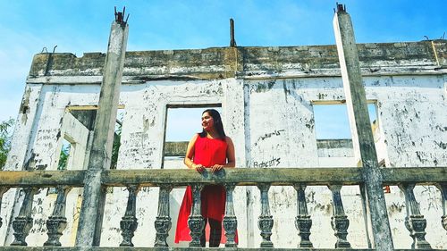 Full length portrait of young woman standing against railing