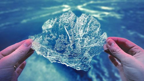 Close-up of hand holding ice against sky