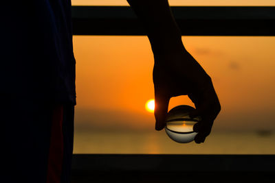 Silhouette woman holding hands against orange sky