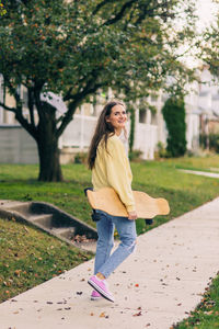 Girl smiling while holding longboard walking on the side walk looking back