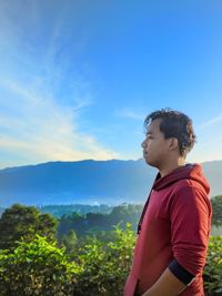 Side view of young man standing against sky