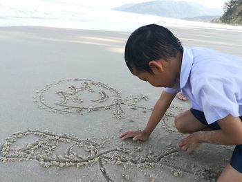 Side view of boy drawing on sand at beach