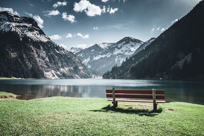 Empty bench by lake against sky