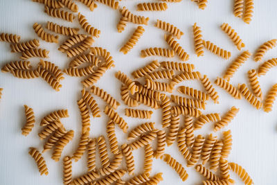 Flat lay of scattered many wavy pasta from whole wheat flour on white table	
