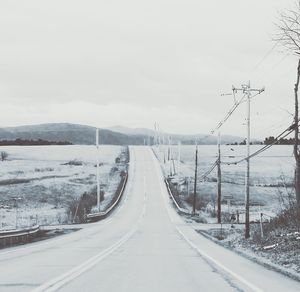 Empty road amidst field against sky