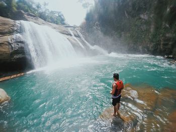 Rear view of man standing against waterfall