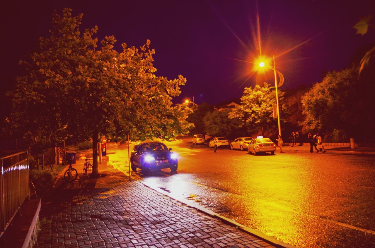 tree, illuminated, the way forward, street light, transportation, lighting equipment, night, road, street, diminishing perspective, vanishing point, footpath, empty, outdoors, sidewalk, car, mode of transport, sky, land vehicle, city