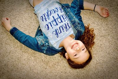 High angle portrait of smiling girl lying on carpet at home