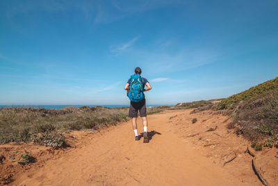 Full length rear view of woman walking on sand at beach against sky