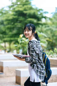 Portrait of smiling young woman standing against trees