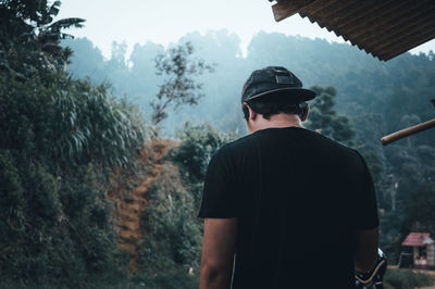 Rear view of man standing by trees against sky