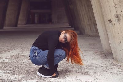 Side view of young woman crouching with eye make-up outdoors