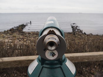 Close-up of coin-operated binoculars by sea against sky