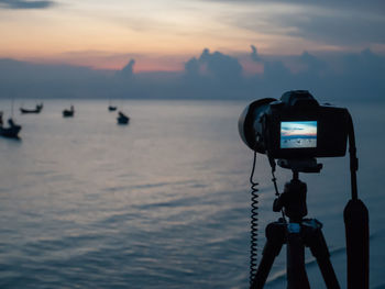 Camera photographing sea against sky during sunset