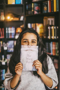 Portrait of girl with long hair holding book near face in bookstore