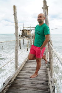 Full length of bald man leaning on pier railing over sea