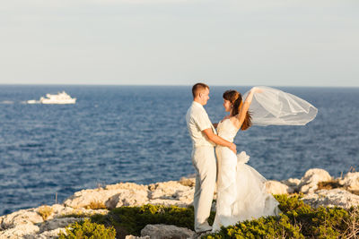 Friends standing on rock by sea against sky