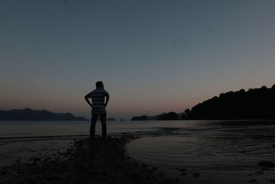 Rear view of silhouette man standing by sea against clear sky