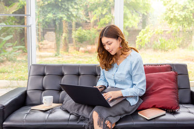Full length of woman using phone while sitting on sofa
