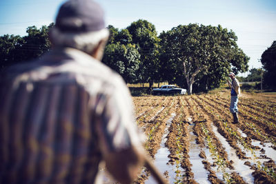 Rear view of farmer looking at coworker standing on field in farm