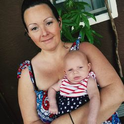 Portrait of smiling mother carrying baby girl against wall