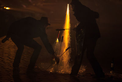 Silhouette people igniting firework on street at night