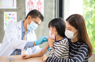 Doctor wearing mask vaccinating girl at clinic