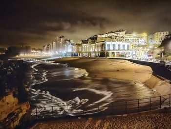 Illuminated buildings by sea against sky in city at night