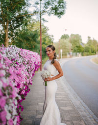 Portrait of bride standing by pink flowers against sky