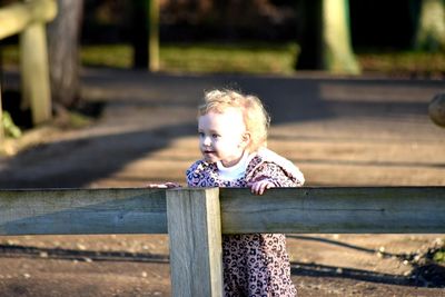 Portrait of cute girl sitting on wooden fence