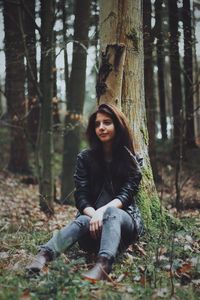 Portrait of young woman sitting on tree trunk in forest