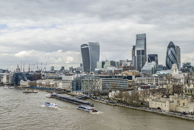 Boats in river by buildings against sky in city