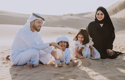 Family playing with sands while sitting at desert