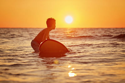 Man swimming in sea against sky during sunset