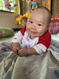 Portrait of cute baby girl sitting on bed at home