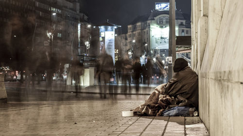 Side view of beggar sitting on sidewalk in city at night