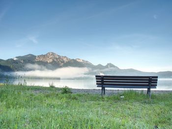 Bench under a tree on a lake shore. mountains at background. take a rest near blue green lake