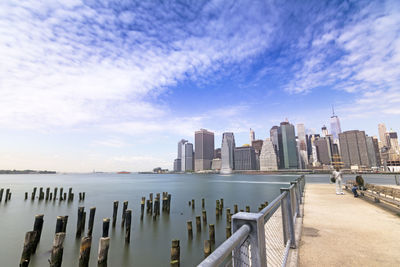 Manhattan skyscrapers by east river against sky seen from pier