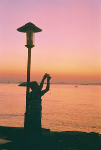 Silhouette person standing on wooden post by sea against sky during sunset