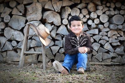 Portrait of smiling boy sitting against stacked wooden logs